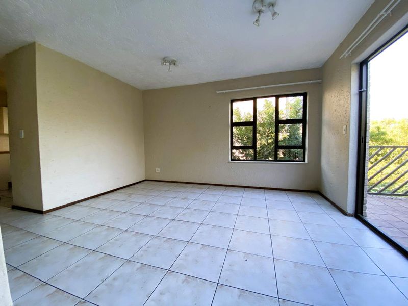 An empty, open-plan living area featuring tiled flooring, large windows for natural light, and direct access to an outdoor balcony space.
