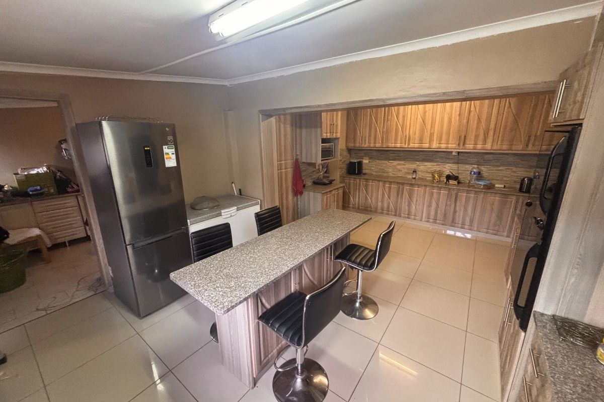 Spacious kitchen featuring wood-look cabinetry, granite-style countertops, a central breakfast island, and tiled flooring, offering a functional layout for cooking and dining.