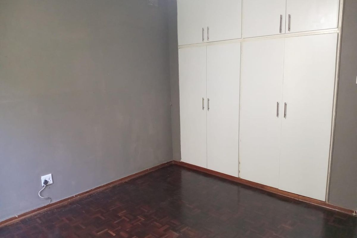 An empty bedroom featuring dark parquet flooring and white built-in cupboards with ample storage space.