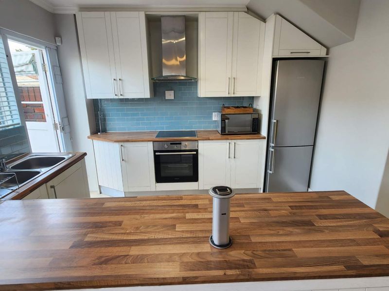 Modern kitchen featuring white cabinetry, wooden countertops, blue tiled backsplash, and integrated stainless steel appliances, including a convenient pop-up power outlet on the island.