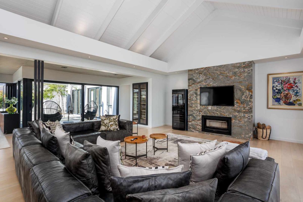 Spacious living room featuring a vaulted ceiling, stone-clad fireplace, integrated wine cooler, and large sliding glass doors opening to an outdoor patio area.