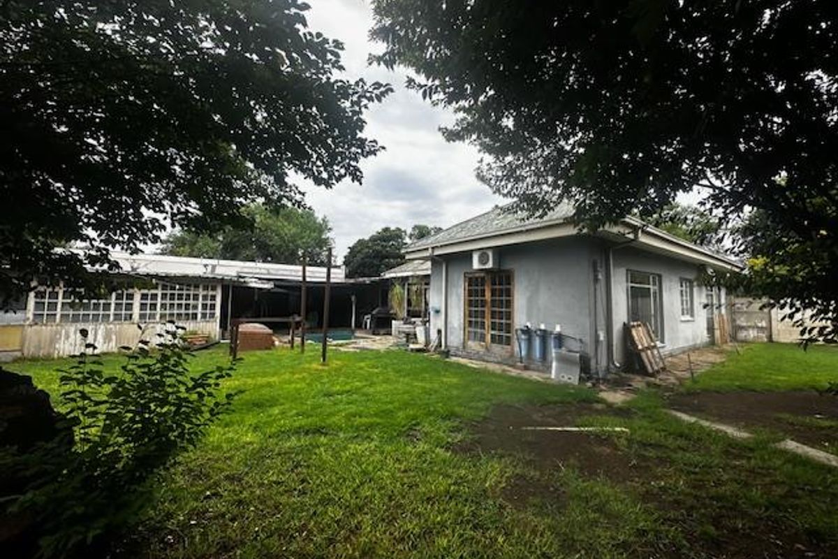Rear view of the property featuring a large lawn, covered patio area, and exterior wall with mounted air conditioning unit.