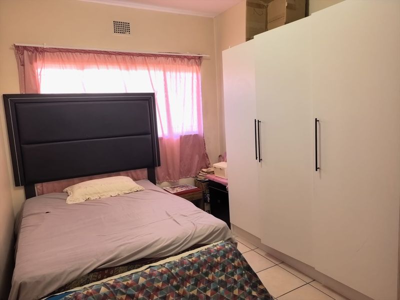 A bedroom featuring tiled flooring and a large white built-in wardrobe providing ample storage space.
