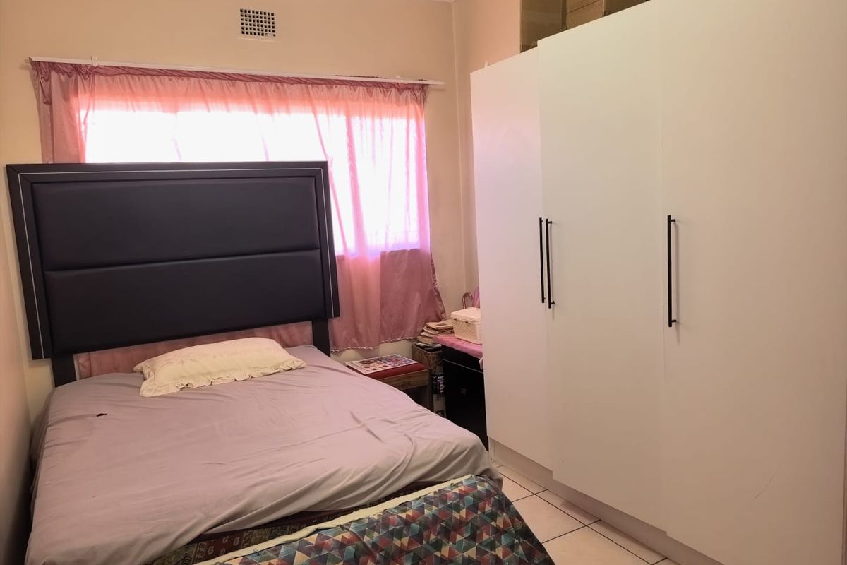 A bedroom featuring tiled flooring and a large white built-in wardrobe providing ample storage space.