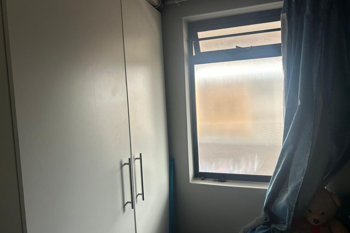 A bedroom featuring a built-in white wardrobe and a window with a metal frame.