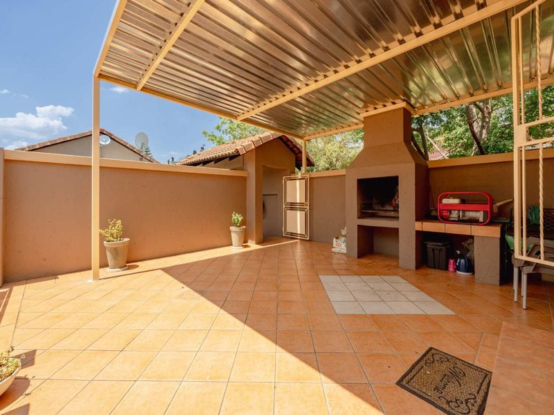 Covered outdoor patio featuring a built-in braai, tiled flooring, and a corrugated metal roof, providing a functional space for outdoor entertaining.