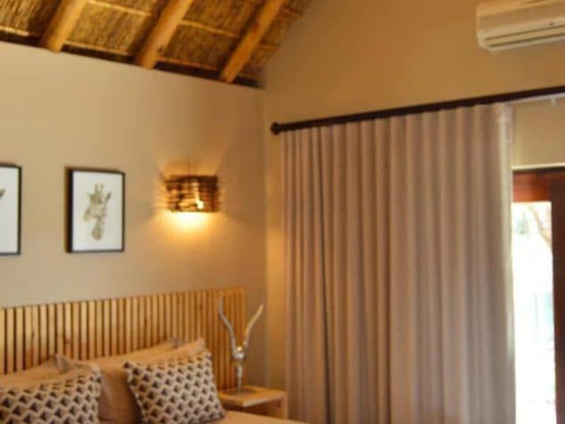 A well-maintained bedroom featuring a high vaulted thatched ceiling with exposed timber rafters, air conditioning, and direct access to an outdoor area.