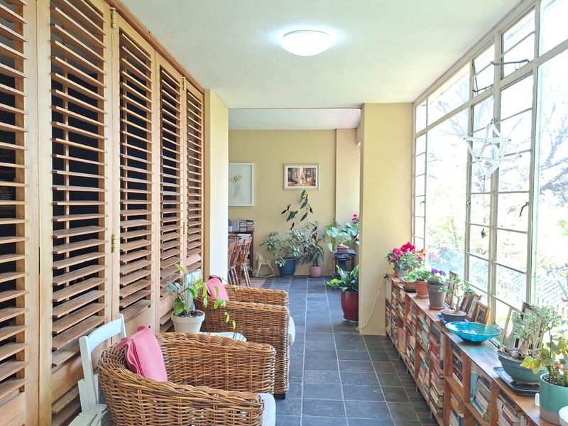 A bright, enclosed balcony featuring slate tile flooring, large steel-framed windows, and extensive built-in timber louvered shutters providing ample storage and character.