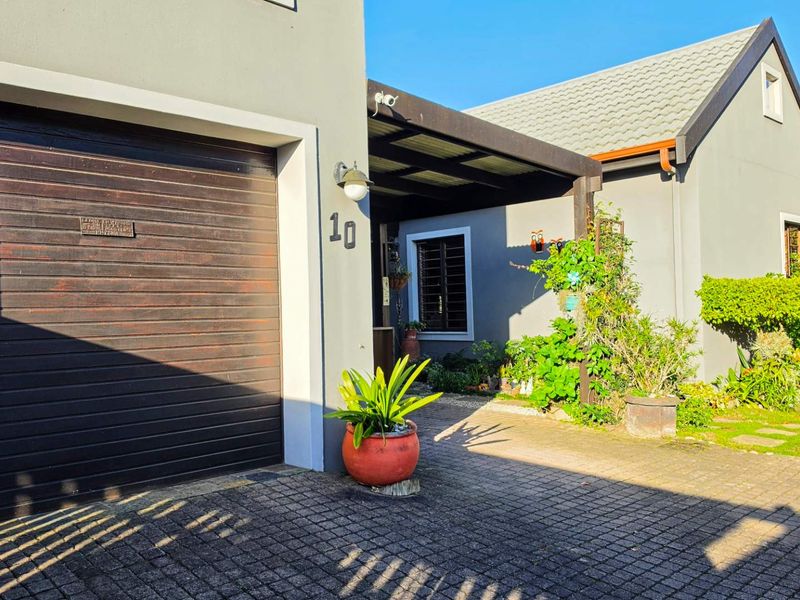 Front elevation of the property featuring a paved driveway, single garage, and a covered entrance area with established garden landscaping.