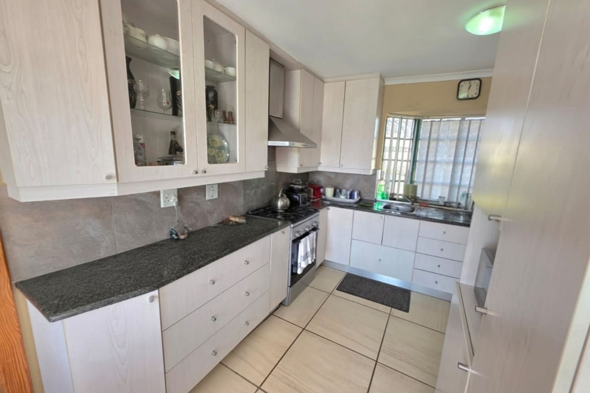 A functional kitchen featuring light wood-finish cabinetry, granite countertops, a tiled backsplash, and a stainless steel extractor fan.