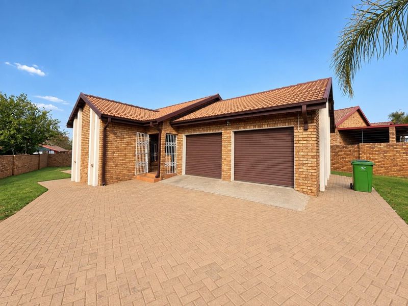 A well-maintained face brick house featuring a double garage with roll-up doors, a paved driveway, and a secure entrance.
