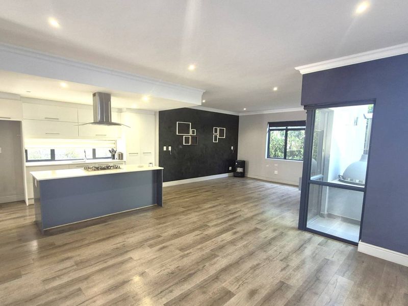 Spacious open-plan living area featuring a modern kitchen with a central island, gas hob, and sleek cabinetry, finished with contemporary laminate flooring.