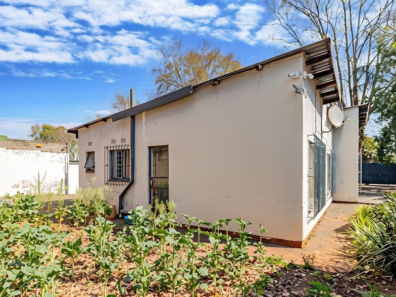 Rear exterior view of the property featuring a paved walkway, security bars on windows, and a garden area.