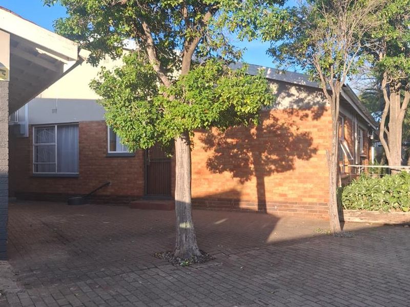 A rear exterior view of the apartment featuring a brick facade, paved courtyard area, and established trees.
