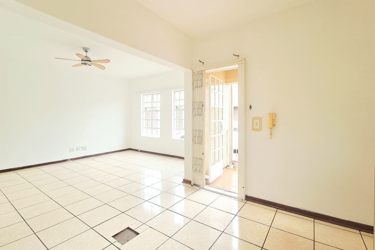 An empty, open-plan living area featuring tiled flooring, a ceiling fan, and a security gate leading to an outdoor space.