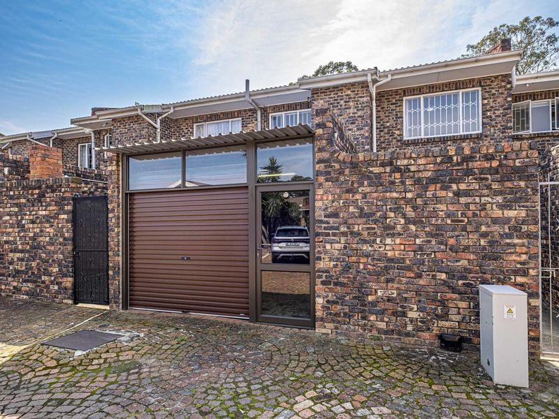 Front elevation of a townhouse featuring a face brick facade, a roller shutter garage door, and a cobblestone driveway.