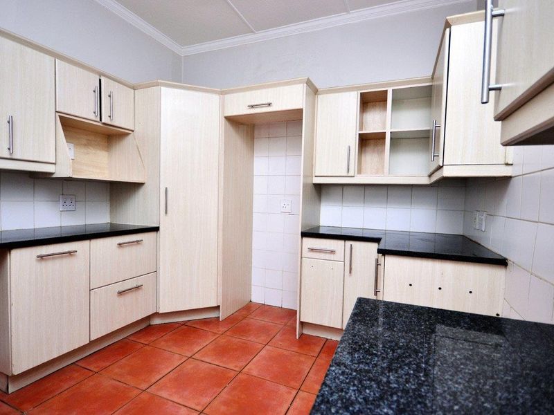 A functional kitchen featuring light wood-finish cabinetry, dark granite countertops, and terracotta-style floor tiles, offering a clean canvas for potential updates.