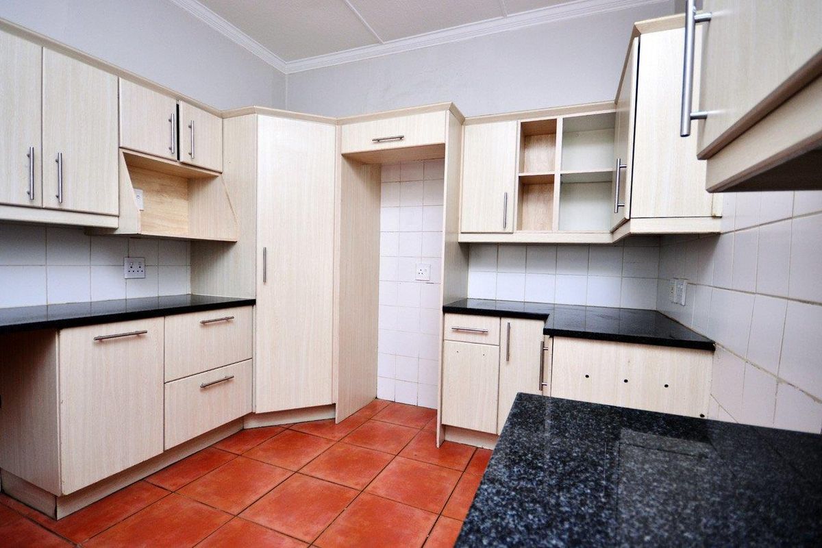 A functional kitchen featuring light wood-finish cabinetry, dark granite countertops, and terracotta-style floor tiles, offering a clean canvas for potential updates.