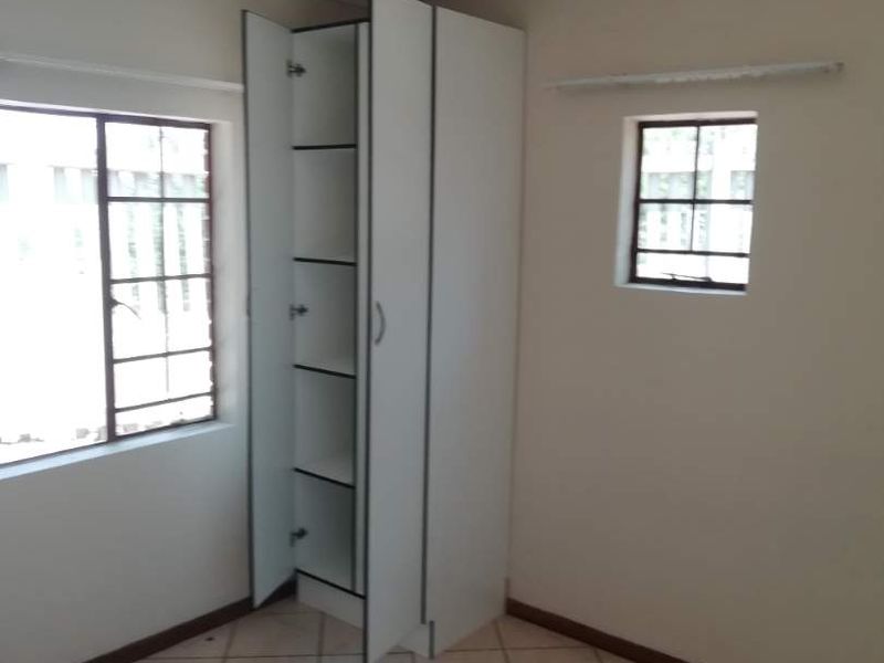 A vacant bedroom featuring tiled flooring, built-in cupboard storage, and steel-framed windows, offering a blank canvas for renovation.