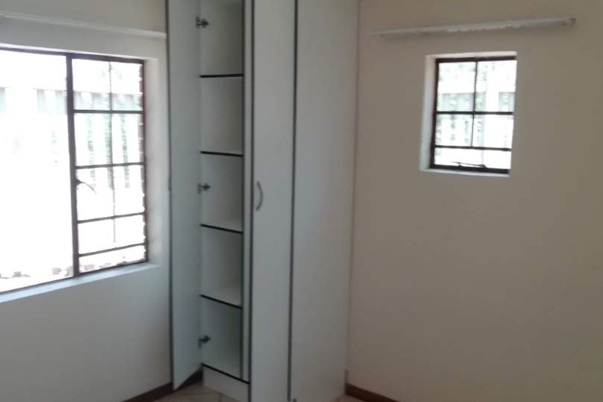 A vacant bedroom featuring tiled flooring, built-in cupboard storage, and steel-framed windows, offering a blank canvas for renovation.
