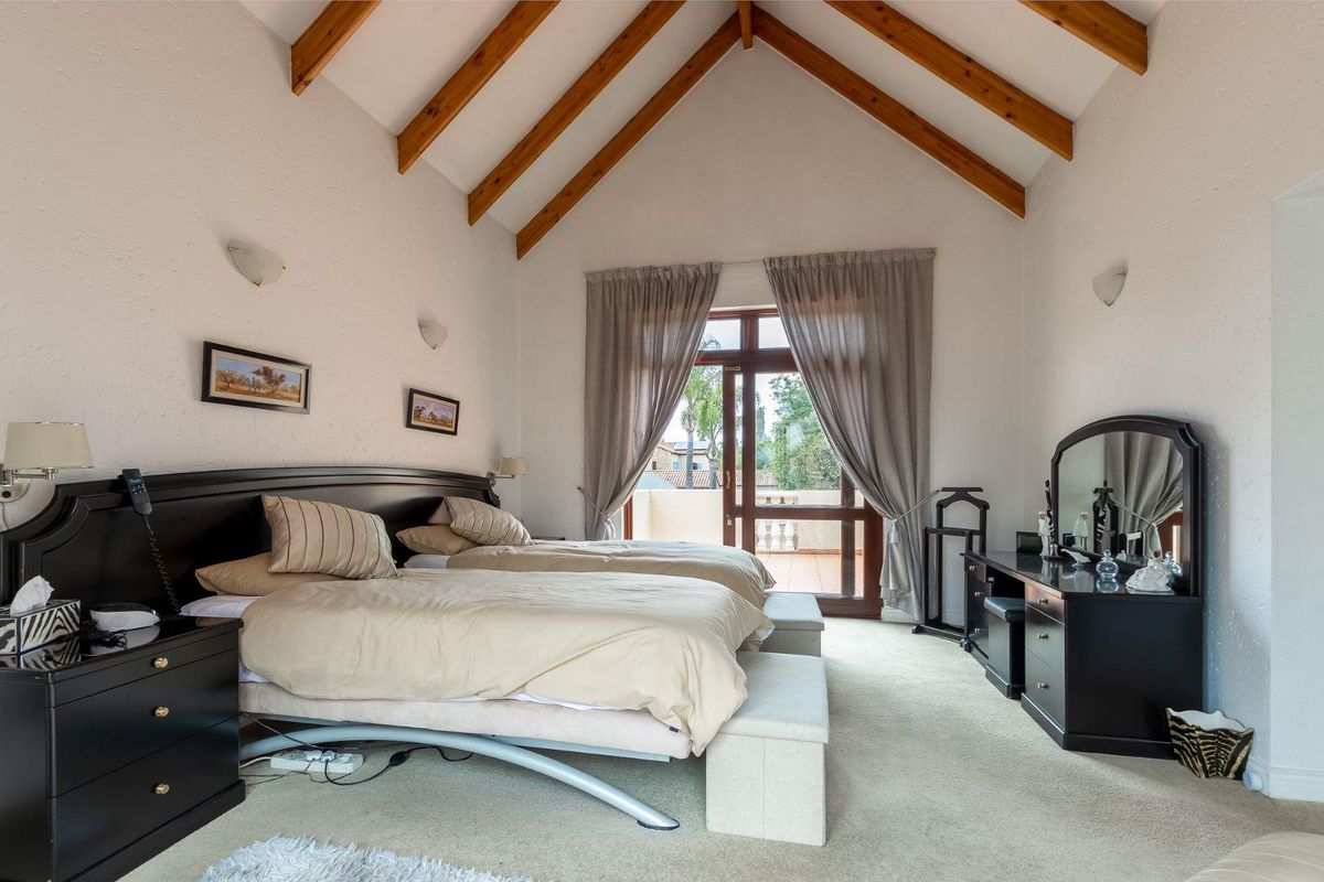 Spacious bedroom featuring a high vaulted ceiling with exposed timber beams and direct access to a private balcony through glass doors.
