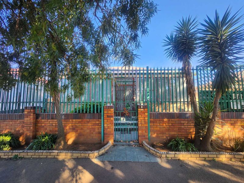 Front elevation of the property featuring a brick boundary wall, metal security fencing, and a gated pedestrian entrance.