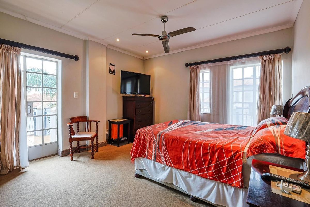 A spacious bedroom featuring neutral carpeting, a ceiling fan, and dual access points to an outdoor balcony area through glass-paned doors.