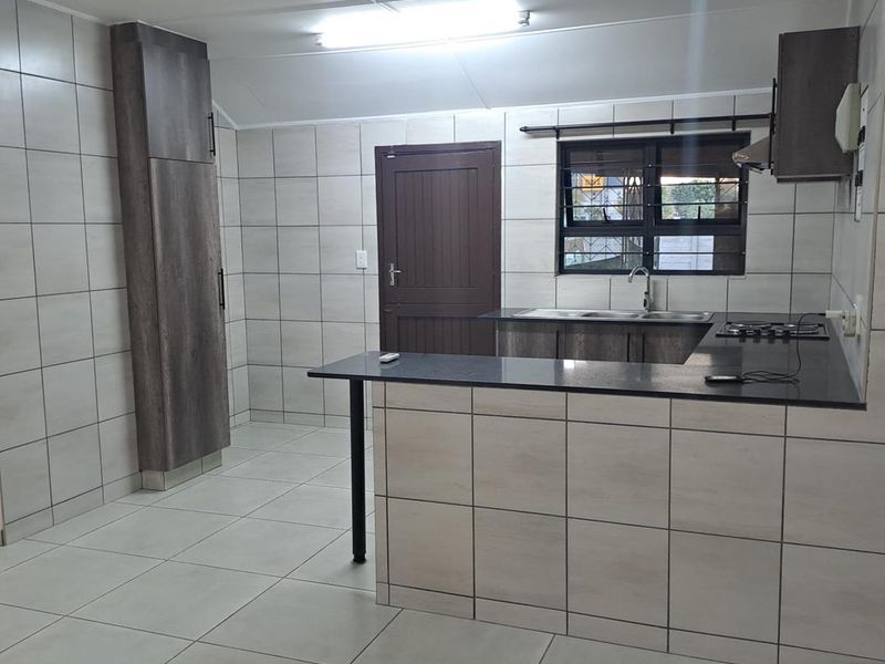 A clean, modern kitchen featuring tiled walls and floors, granite countertops, built-in cabinetry, and a gas hob with an extractor fan.