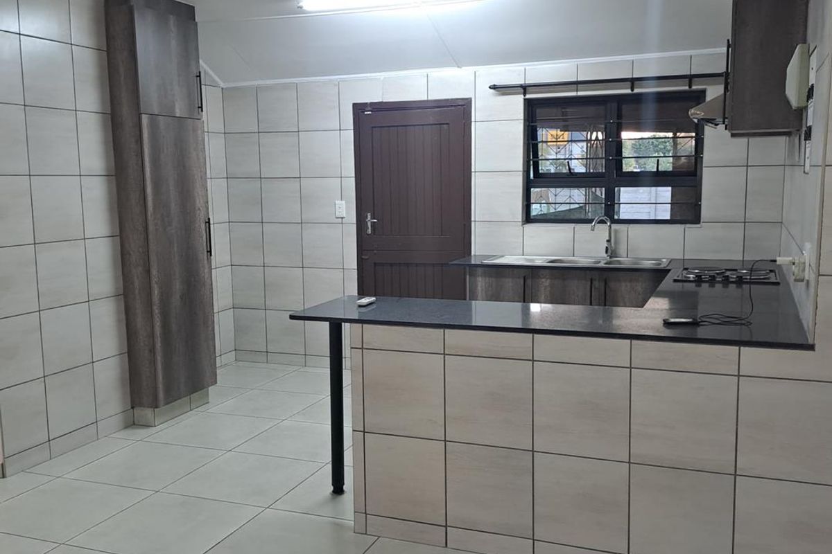 A clean, modern kitchen featuring tiled walls and floors, granite countertops, built-in cabinetry, and a gas hob with an extractor fan.