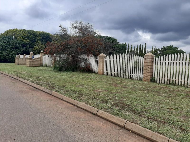 Street view of the property boundary featuring a brick and picket fence perimeter along the asphalt road.