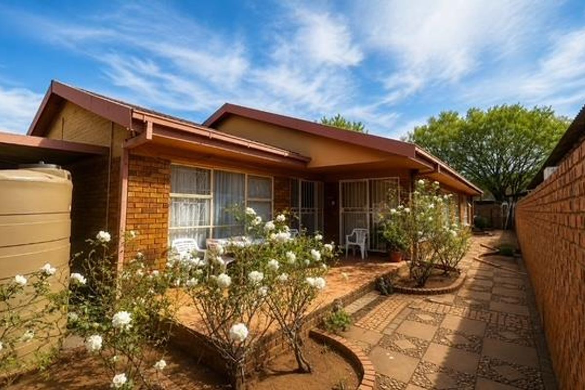 Rear view of the property featuring a brick facade, a covered patio area, a paved walkway, and a large water storage tank.