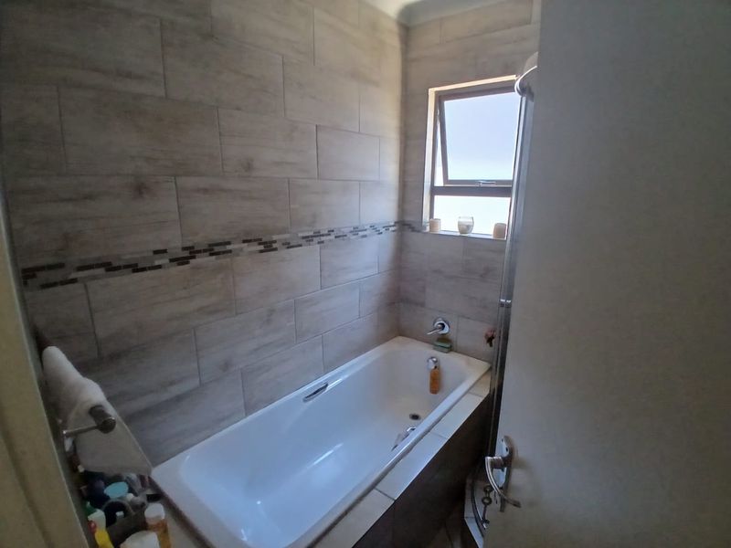 A compact bathroom featuring a built-in bathtub with modern wood-look wall tiles and a decorative mosaic border.