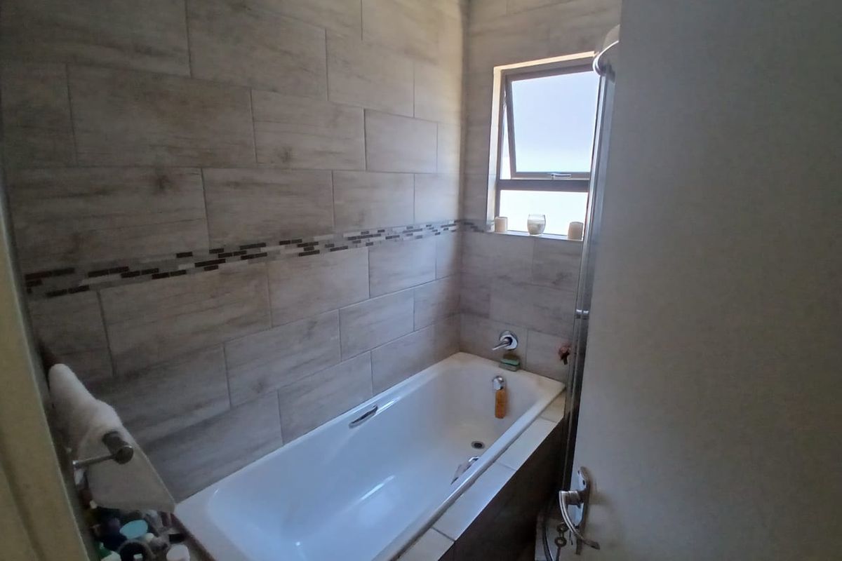 A compact bathroom featuring a built-in bathtub with modern wood-look wall tiles and a decorative mosaic border.