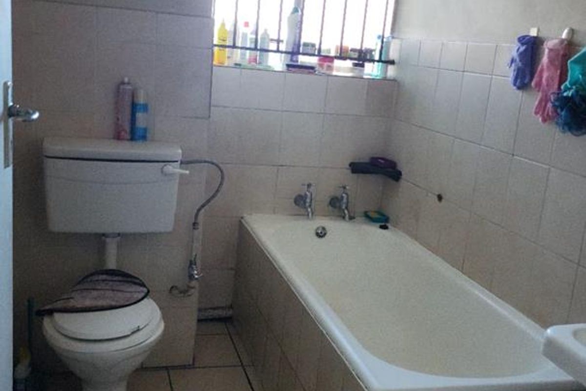 A functional bathroom featuring a standard bathtub, toilet, and tiled walls with a security-barred window for ventilation.