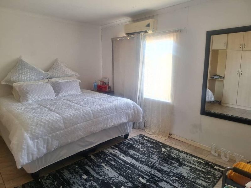 A functional bedroom featuring tiled flooring, built-in cupboards, and a wall-mounted air conditioning unit.