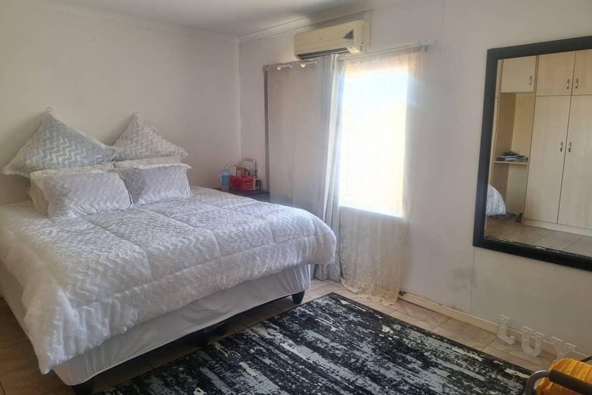 A functional bedroom featuring tiled flooring, built-in cupboards, and a wall-mounted air conditioning unit.