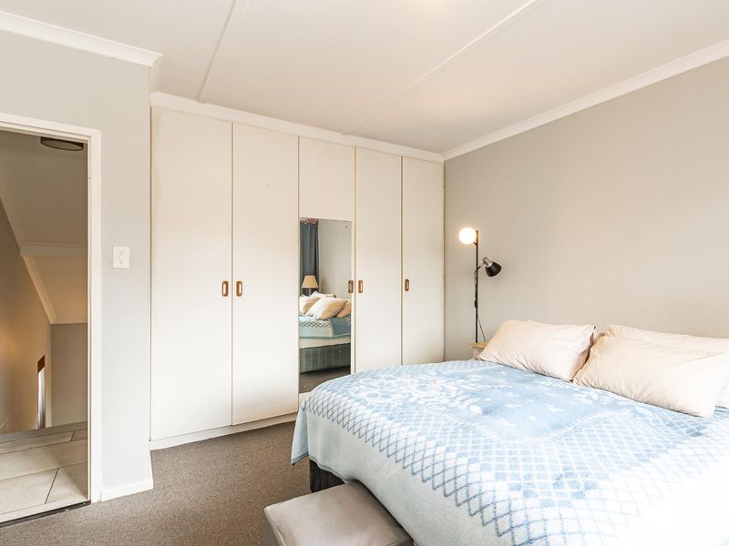A well-maintained bedroom featuring neutral walls, carpeted flooring, and extensive built-in cupboards with a central mirrored panel.