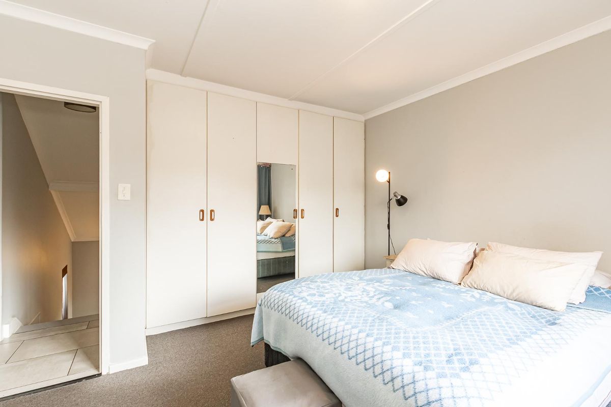 A well-maintained bedroom featuring neutral walls, carpeted flooring, and extensive built-in cupboards with a central mirrored panel.