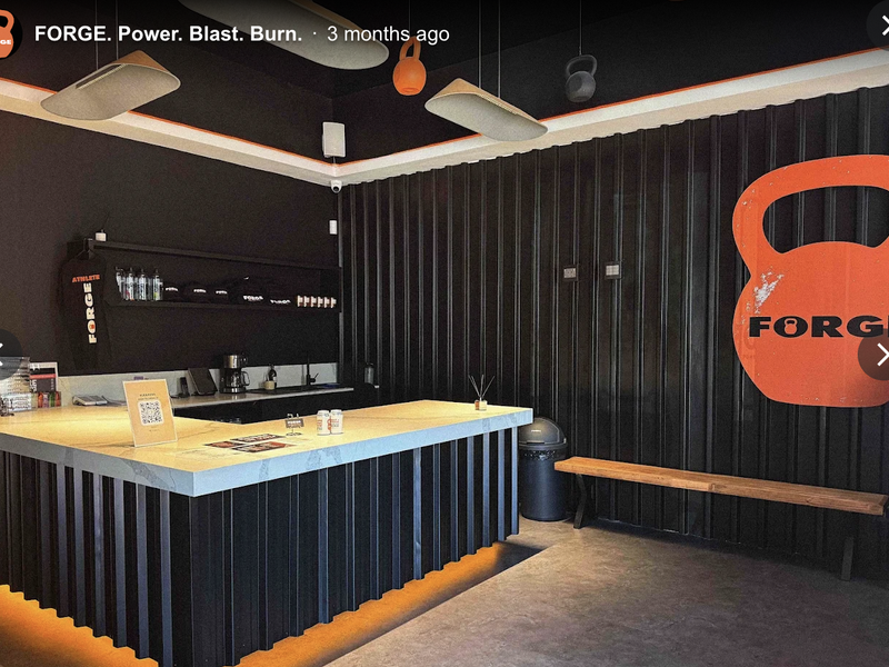 A modern gym reception area featuring a custom built-in counter, industrial-style corrugated metal wall cladding, and integrated ambient LED lighting.