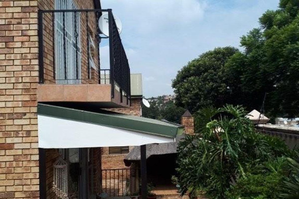 Side view of the cluster property featuring a brick facade, a covered patio area, and an upper-level balcony with metal railings.