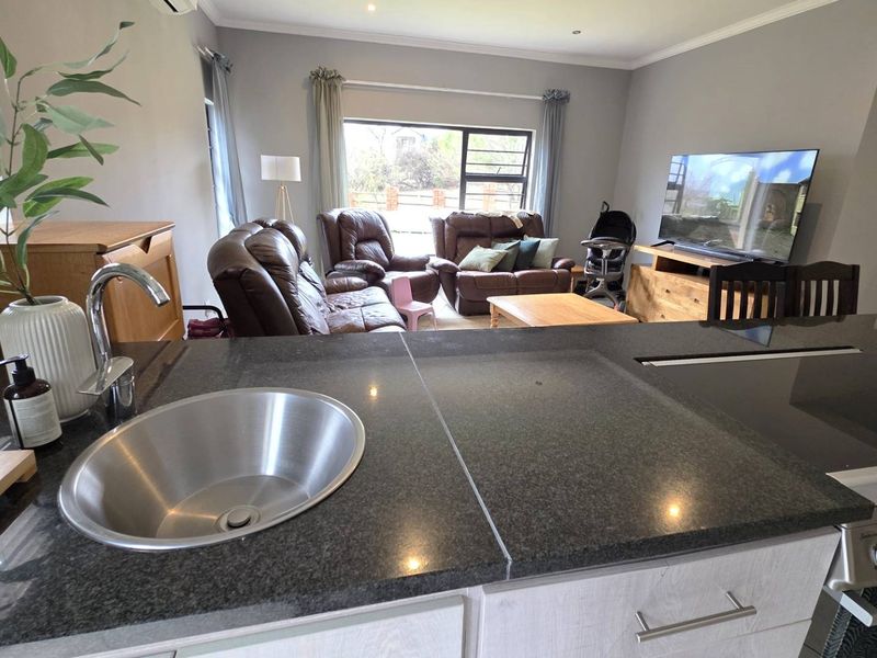 Open-plan living area featuring a modern kitchen with granite countertops, integrated sink, and built-in stove, flowing into a comfortable lounge space.