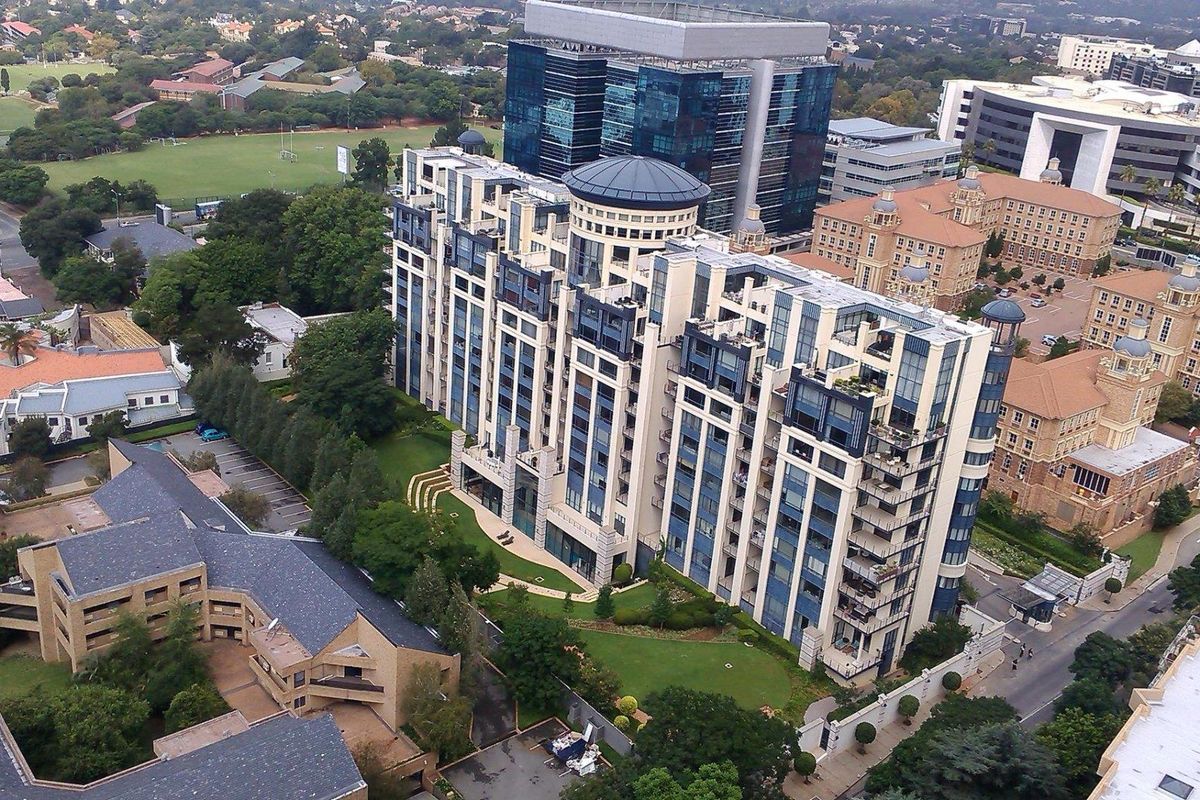 An aerial view of a modern multi-story apartment complex situated in a well-developed urban area with landscaped grounds and surrounding infrastructure.
