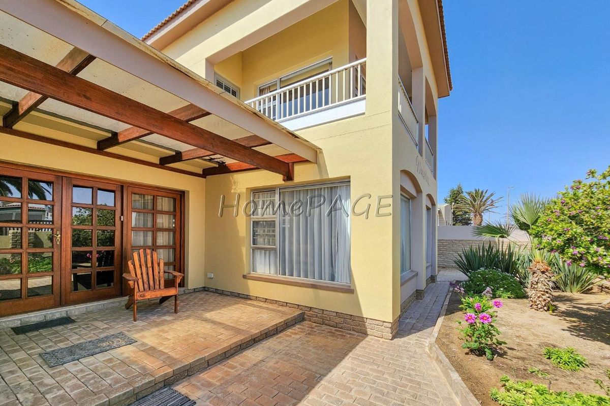 A rear view of the house featuring a paved patio area with a timber pergola, leading to a small garden and an upper-level balcony.