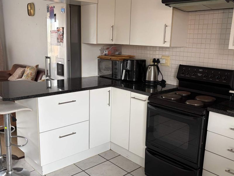 A functional kitchen featuring white cabinetry, black granite countertops, a tiled backsplash, and a freestanding electric stove with an extractor fan.