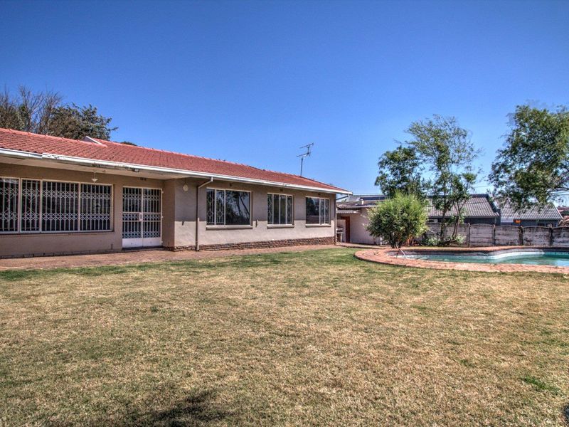 Rear view of the property featuring a spacious lawn, a swimming pool, and a paved patio area adjacent to the main house structure.