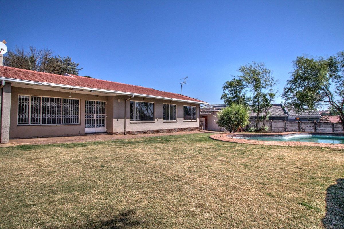 Rear view of the property featuring a spacious lawn, a swimming pool, and a paved patio area adjacent to the main house structure.