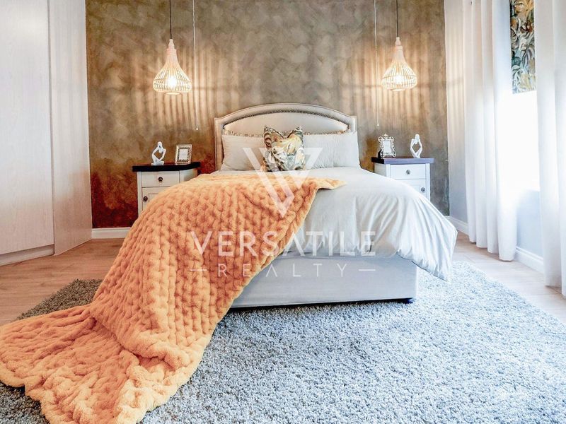 A well-maintained bedroom featuring laminate flooring, built-in wardrobes, and decorative pendant lighting against a textured feature wall.