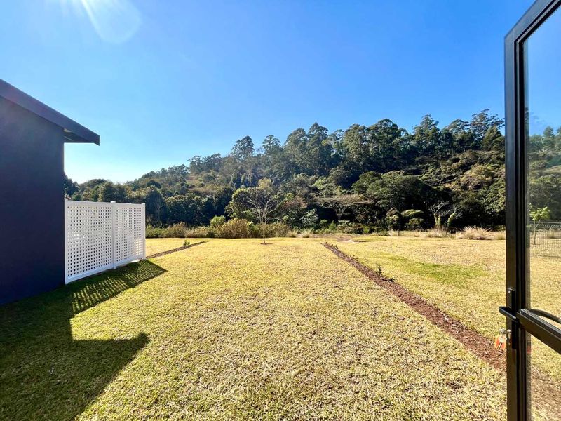 A view of the rear garden featuring a manicured lawn, white privacy screening, and direct access through a modern black-framed glass door.