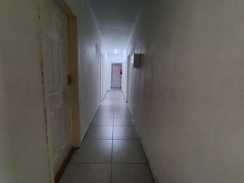 A long, narrow hallway featuring neutral tiled flooring and multiple interior doors, providing access to various rooms within the property.