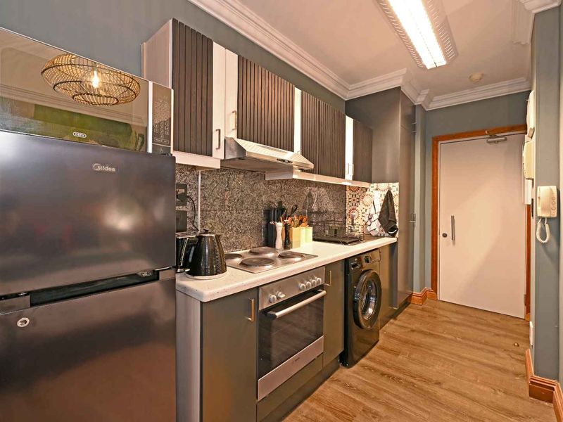 A compact, modern kitchen featuring dark cabinetry, stone countertops, integrated oven and hob, and durable laminate flooring with a neutral wall finish.